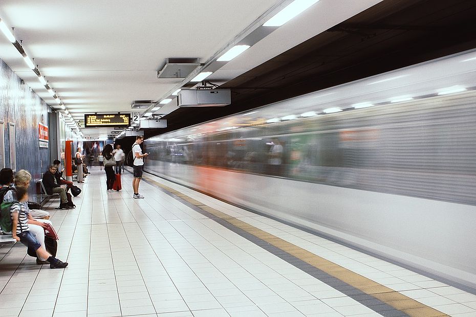 U-Bahn fährt durch Haltestelle, am Bahnsteig stehen Menschen