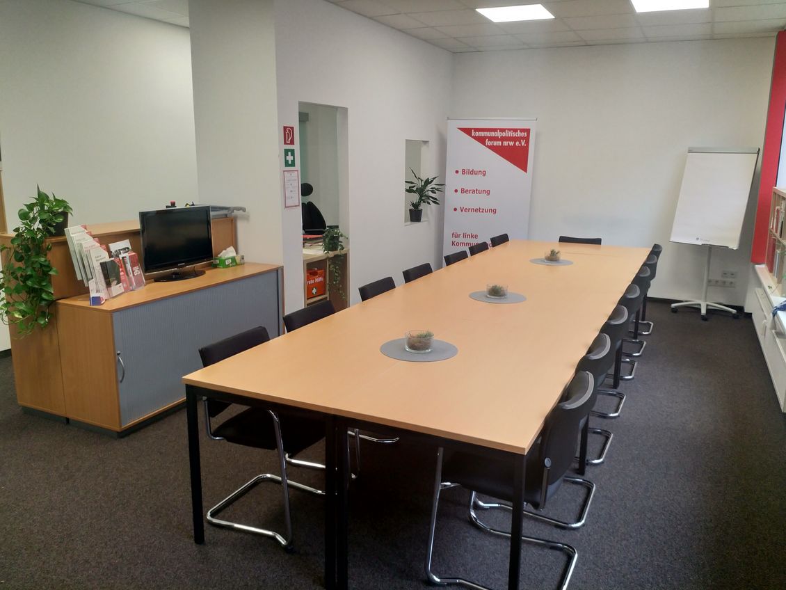 Raum mit Konferenztisch in der Mitte und weiteren Büromöbeln